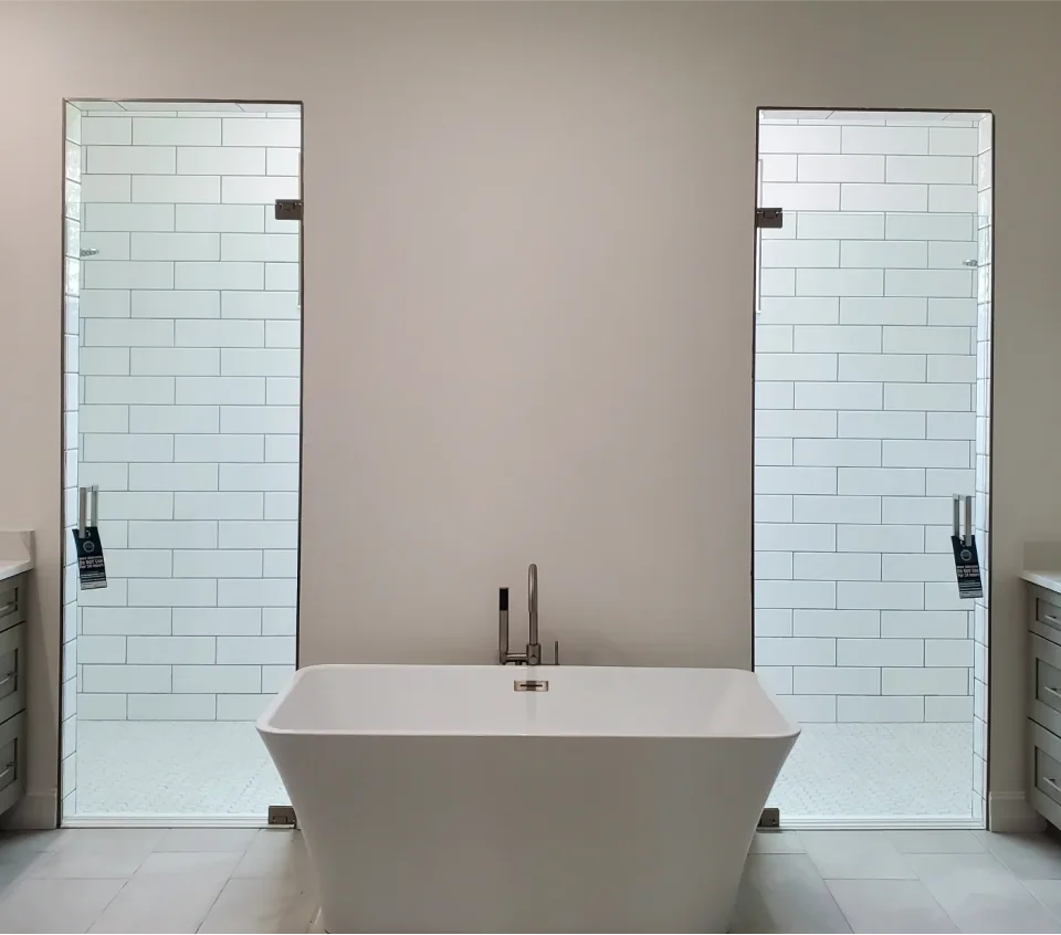 Minimalist bathroom with a white freestanding bathtub centered against a wall. Two glass-enclosed showers with white subway tile are on either side.