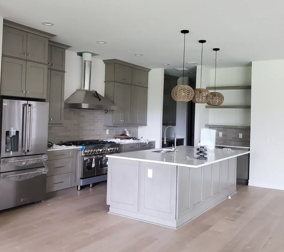 Modern kitchen with gray cabinets, a central island, stainless steel appliances, and pendant lights. Wood flooring and light-colored walls enhance the open space.